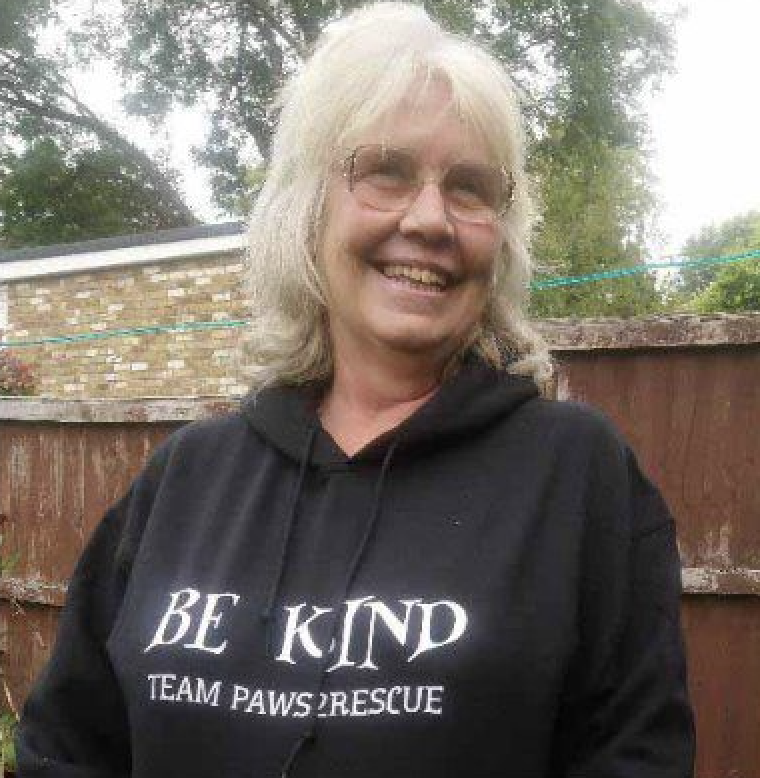 A photo of Paws2Rescue team member Karen standing outside and smiling while wearing a Paws2Rescue hoodie with the words "Be Kind" printed on the front
